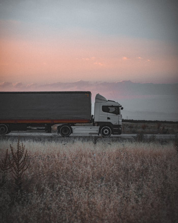 a-trailer-truck-on-the-road-5410923 A cargo truck travels on a highway at sunset, surrounded by an open landscape, symbolizing logistics and transportation.